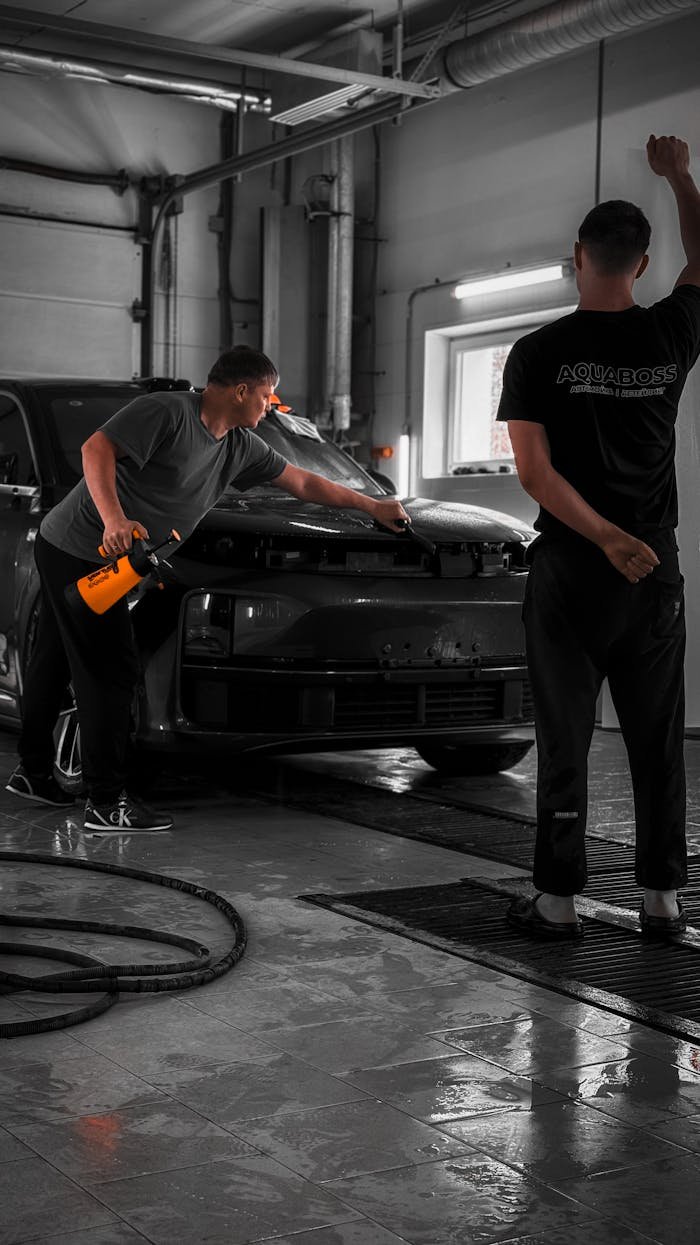 Two men detailing a car in a professional garage with focused cleaning tools.